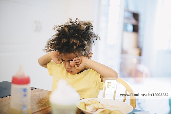Boy rubbing eyes while sitting at table