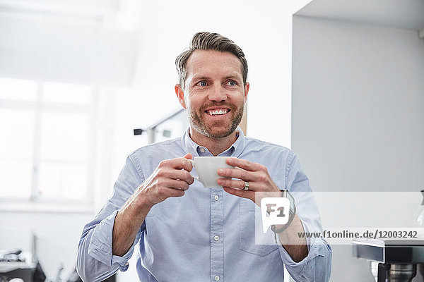 Smiling businessman holding coffee cup while standing at creative office