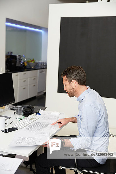 Seitenansicht des Architekten bei der Analyse von Bauplänen am Schreibtisch im Kreativbüro