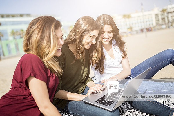 Drei glückliche Freundinnen mit einem Laptop am Strand