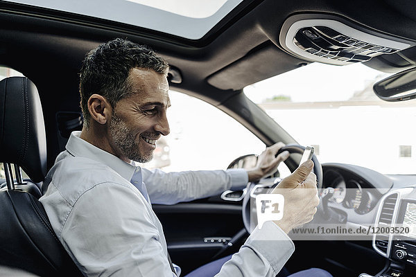 Businessman driving car looking at cell phone