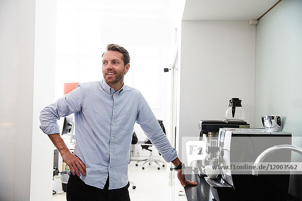 Businessman standing by coffee maker at counter in creative office