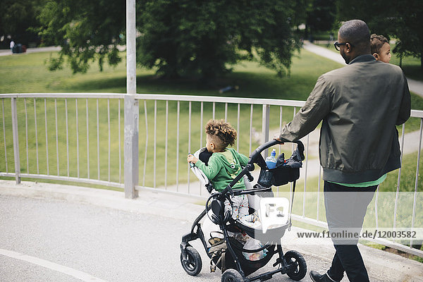 Father walking with children while pushing baby stroller on bridge