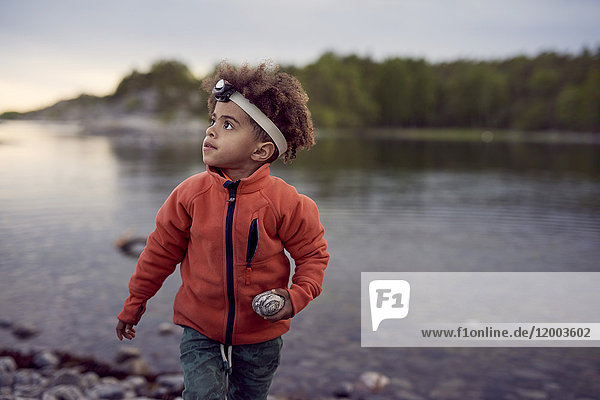 Junge trägt eine Stirnlampe  die bei Sonnenuntergang Felsen am Strand hält.