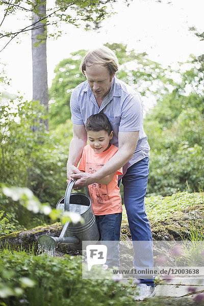 Vater und Sohn gießen Pflanzen mit Dose im Hinterhof