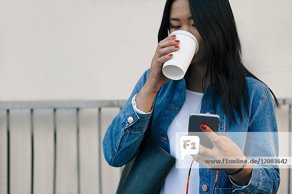 Teenage girl drinking coffee while using mobile phone