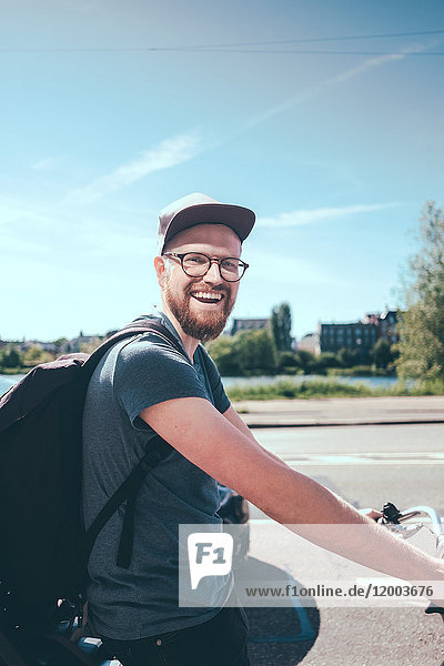 Seitenansicht Porträt eines glücklichen Mannes mit Rucksack beim Radfahren auf der Straße gegen den Himmel