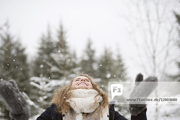 Glückliche junge Frau genießt Schneefall im Winterwald