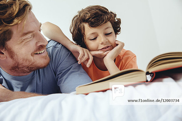 Father and son reading book in bed
