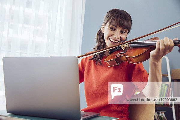 Woman using laptop to play a song on a violin