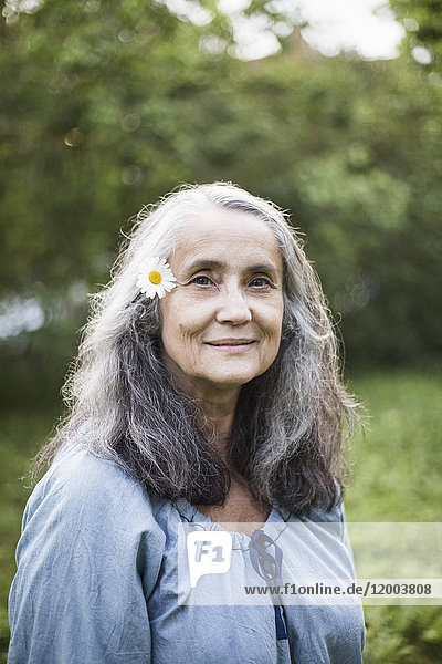 Porträt der lächelnden Seniorin mit Gänseblümchen im Hinterhof