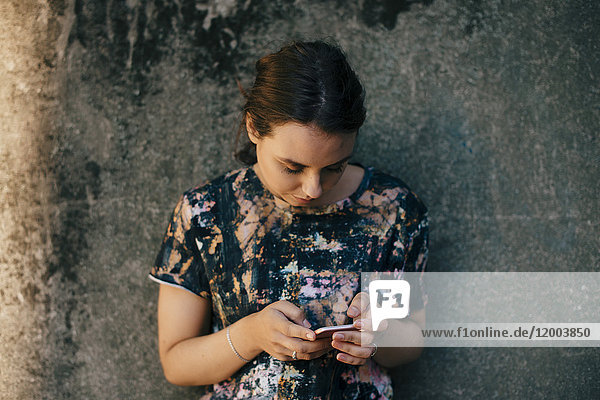 Young woman using mobile phone against wall