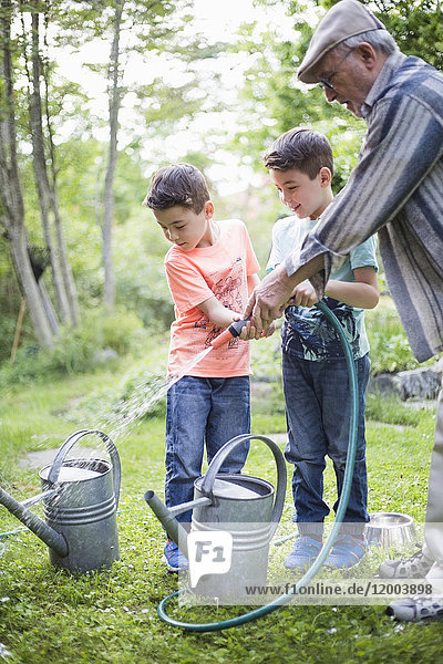 Grandfather with grandsons holding garden hose while filling watering cans in back yard