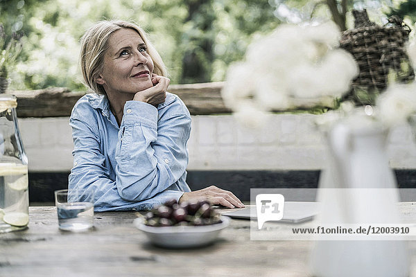Mature woman sitting on terrace  with cherries on table