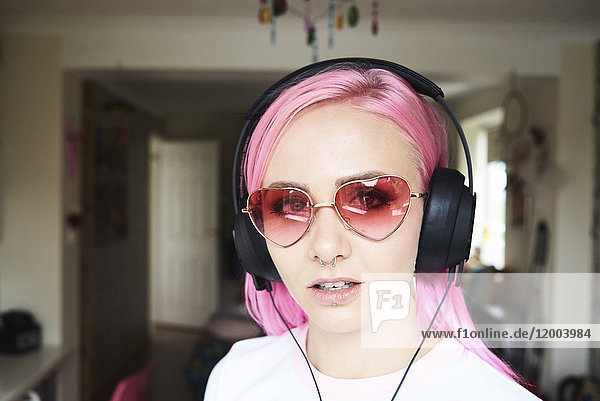 Portrait of young woman with pink hair and heart-shaped sunglasses listening to music