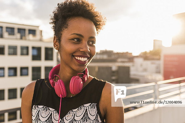 Portrait der glücklichen jungen Frau mit Kopfhörer auf dem Dach