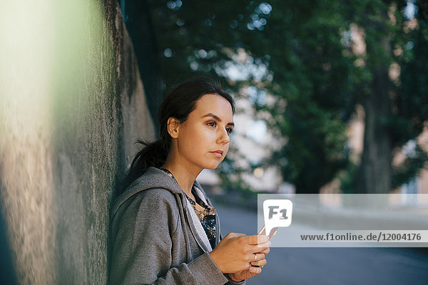 Seitenansicht einer jungen Frau  die ein Smartphone in der Hand hält  während sie wegschaut.