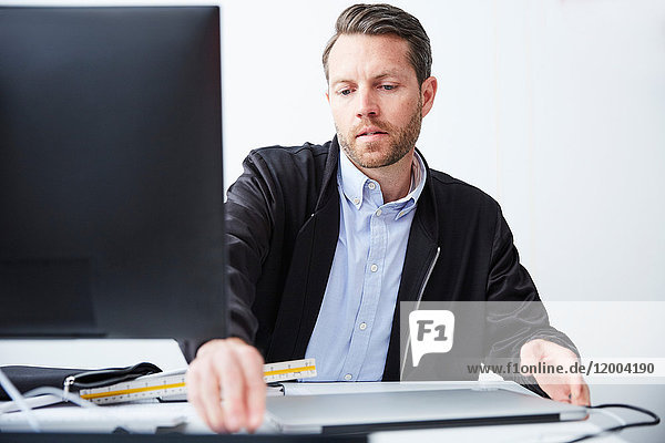 Serious architect using computer at desk in creative office