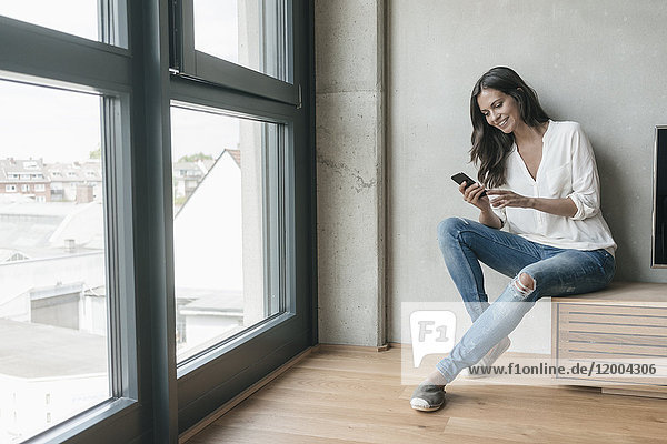 Lächelnde Frau im Sitzen mit Blick auf das Handy