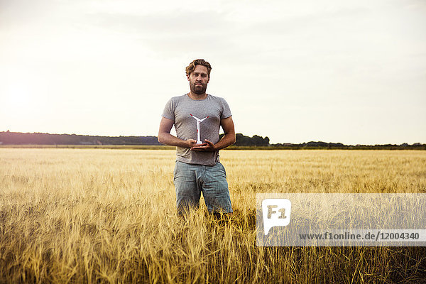Mann steht im Getreidefeld und hält eine Miniatur-Windkraftanlage.