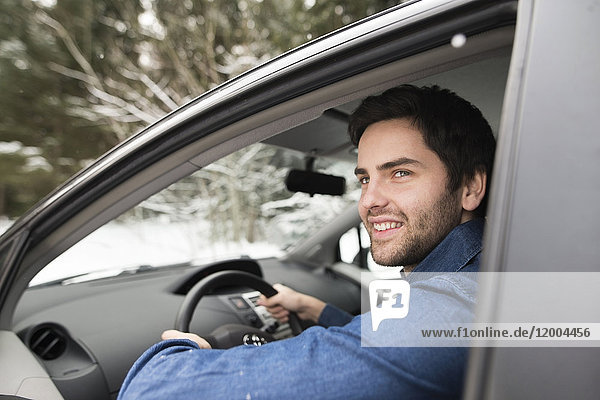 Portrait of smiling young man driving car in winter