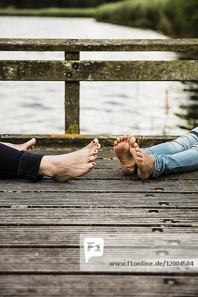 Feet of mother and daughter on jetty at a lake