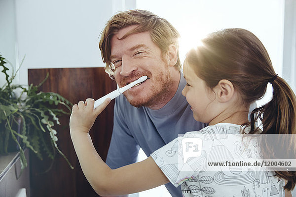 Daughter brushing her father?s teeth in bathroom