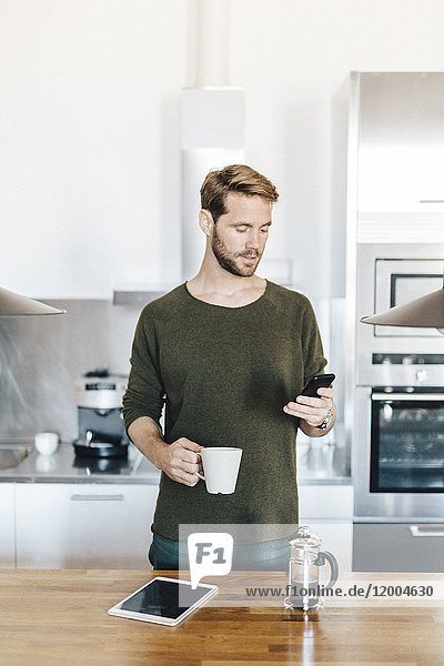 Porträt eines in der Küche stehenden Mannes mit Blick auf das Handy