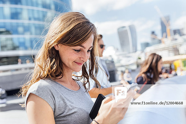 UK  London  smiling woman checking her smartphone