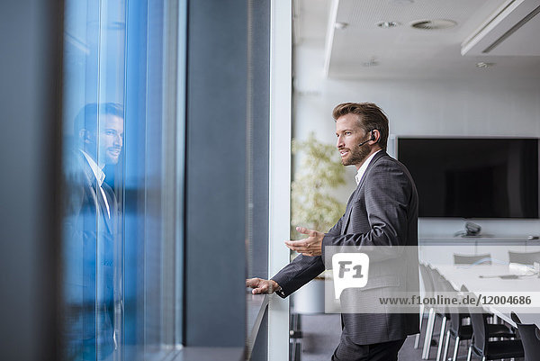 Relaxed businessman with bluetooth headset standing in his office looking out of the window