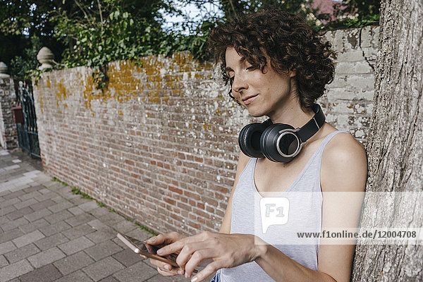 Frau mit Kopfhörer und Handy auf dem Bürgersteig