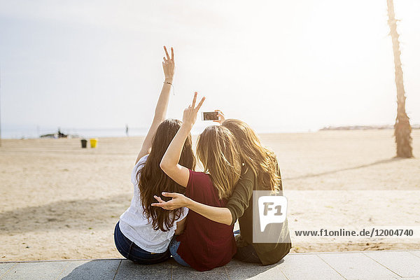 Rückansicht von drei Freundinnen am Strand mit einem Selfie