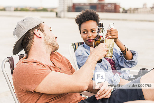 Young couple clinking beer bottles on rooftop