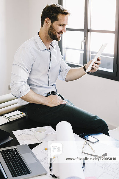 Architect sitting on desk in his office using tablet