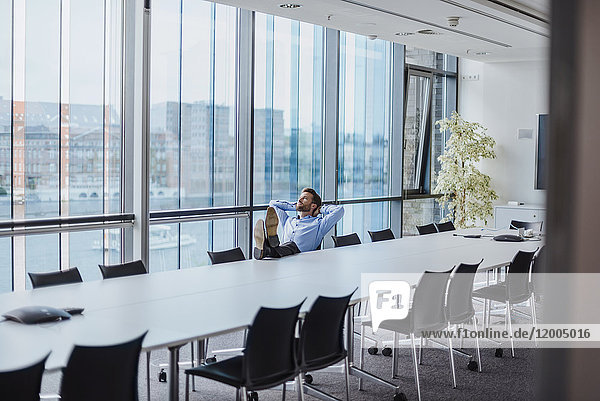 Deutschland  Berlin  Geschäftsmann sitzend im Konferenzraum mit den Füßen nach oben aus dem Fenster schauend