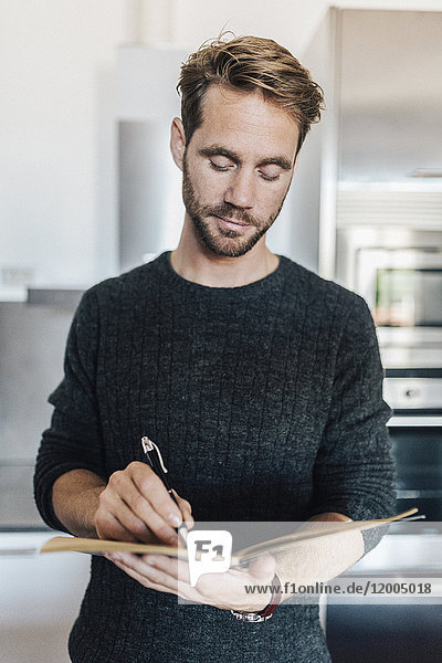 Porträt eines Mannes  der in einem Notizbuch in der Küche schreibt.