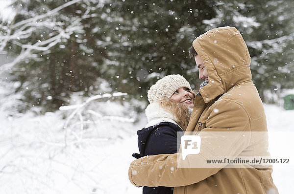 Fröhliches junges Paar im schneebedeckten Winterwald gegenüber stehend