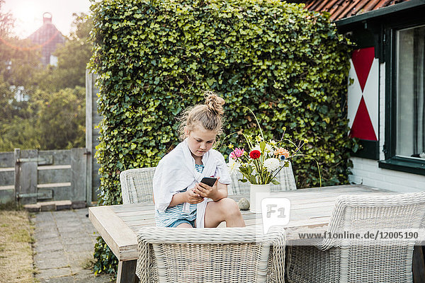 Mädchen sitzend auf dem Terrassentisch mit Handy