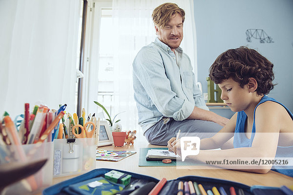 Father helping boy doing his schoolwork at home