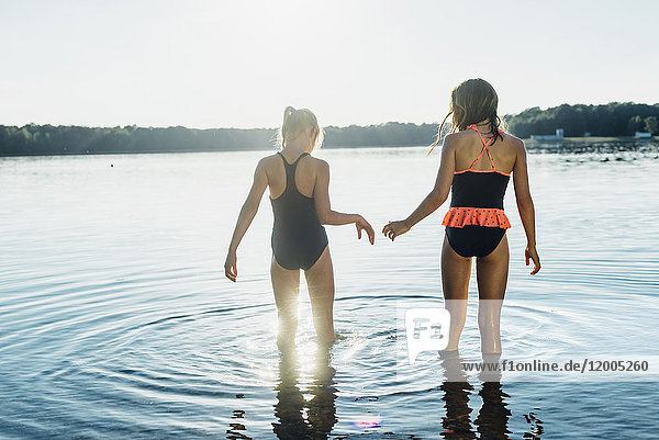 Back view of two friends wearing swimsuits standing at lakeshore