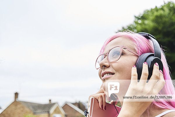 Junge Frau mit rosa Haaren beim Musikhören im Freien