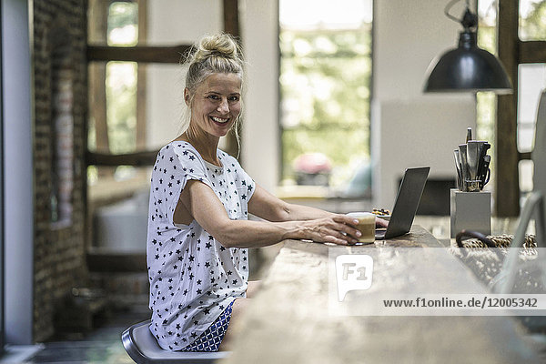 Woman sitting in kitchen  using laptop