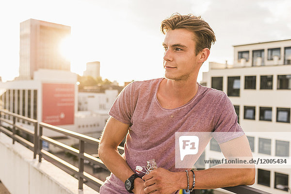 Young man with beer bottle on rooftop at sunset