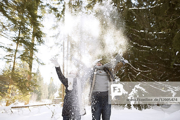 Glückliches junges Paar  das Schnee in die Luft wirft.