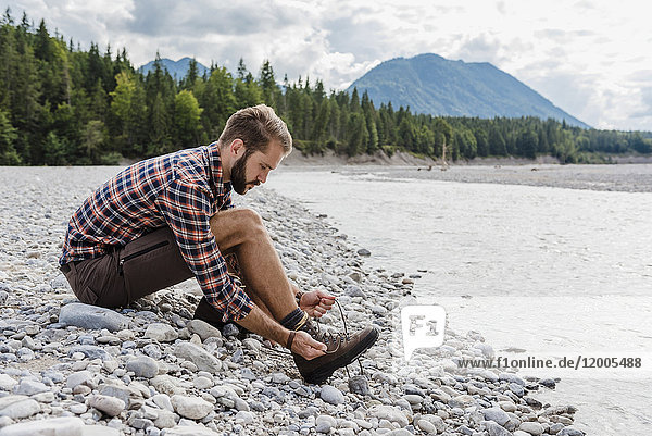 Germany  Bavaria  hiker sitting at riverside tying his shoe