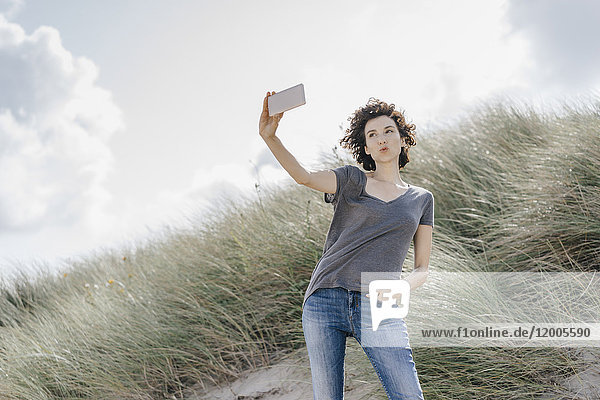 Frau steht in der Stranddüne und nimmt einen Selfie.