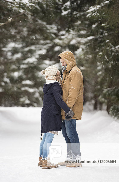Fröhliches junges Paar steht sich gegenüber in verschneiter Winterlandschaft