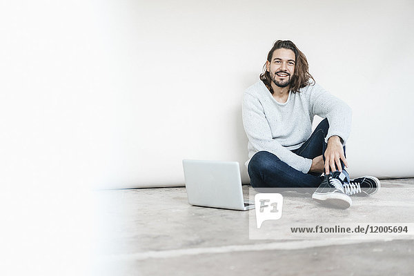 Porträt eines lächelnden Mannes mit Laptop auf dem Boden sitzend