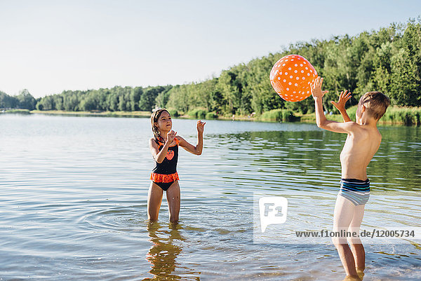 Boy and girl standing at lakeshore playing with beach ball