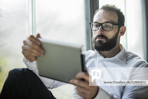 Businessman sitting by window  using digital tablet